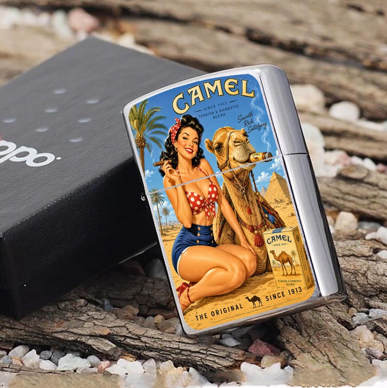 May include: A silver-colored Zippo lighter with a vintage Camel cigarettes graphic. The graphic features a woman in a polka dot bikini and shorts, a camel smoking a cigar, and the text "CAMEL" and "SINCE 1913". The lighter is in a black box.