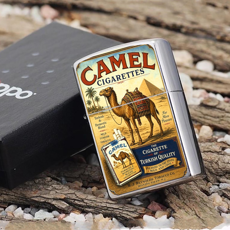 Puede incluir: Un encendedor Camel Cigarettes plateado con un dise&ntilde;o vintage. El encendedor presenta una ilustraci&oacute;n de camello con una pir&aacute;mide y palmeras. La caja es negra con la palabra "Zippo". El encendedor est&aacute; sobre un lecho de virutas de madera.