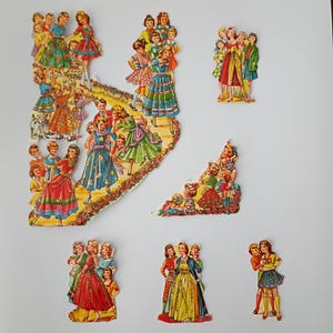 May include: A collection of vintage-style paper cutouts featuring groups of figures in colorful dresses and outfits. The illustrations depict various scenes of people in patterned clothing, including floral and solid-colored skirts and dresses.