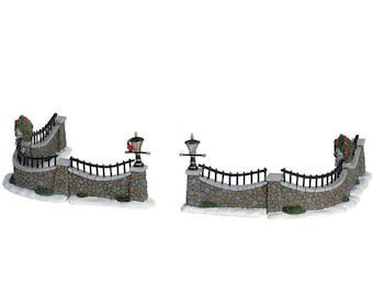 May include: A set of two stone wall sections with black metal fencing and decorative lamp posts. Each section has a curved shape and is made of grey stone with green foliage.