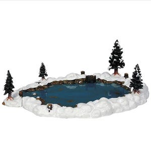 May include: A miniature winter scene with a blue pond, snow, and evergreen trees. A small bridge spans the pond. This decorative item is likely for a festive display, evoking a winter landscape.