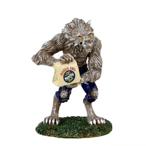 Puede incluir: Una figurita de hombre lobo sosteniendo una bolsa de papel marrón con el texto "Doggie Bag The Full Moon Diner" impreso en ella. El hombre lobo está de pie sobre una base verde.