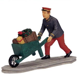 May include: A man in a blue uniform and red pants pushes a green wheelbarrow filled with wrapped gifts and a small Christmas tree.