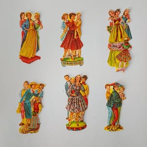 Może przedstawiać: Sześć wycinanek papierowych lalek w stylu vintage, przedstawiających różne postacie w kolorowych strojach z połowy wieku. Ilustracje ukazują grupy osób w sukienkach, garniturach i strojach codziennych, niektóre na małych podstawkach.