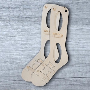 May include: Two wooden sock blocking forms, labeled "WILD-Stitchers" and "M" for size medium. The forms have a cutout for the heel and toe of a sock.