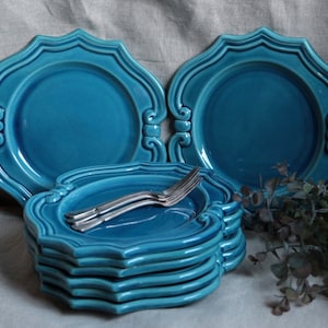 Può includere: Un set di sei piatti da portata in ceramica blu turchese con un bordo decorato a festoni. I piatti sono impilati uno sopra l'altro, con un set di forchette d'argento sopra la pila.
