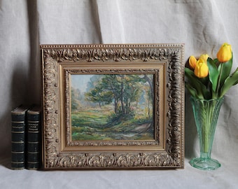 May include: An antique landscape painting in a gold ornate frame. The artwork depicts a serene forest scene with trees, a stream, and a grassy area. A vase of yellow tulips and two vintage books are also present.
