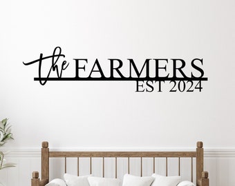 May include: Black metal wall sign with the text "The Farmers Est 2024" in a modern font. The sign is mounted on a white wall above a wooden bench with white cushions.