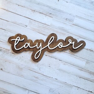 May include: A wooden sign with the name "Taylor" written in white cursive lettering.