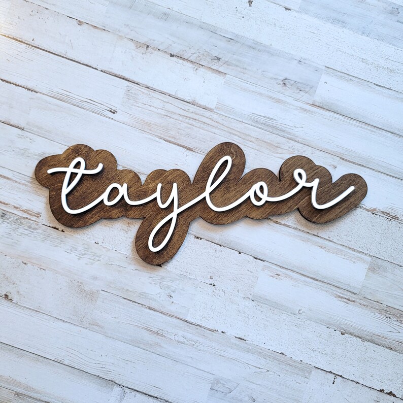 May include: A wooden sign with the name "Taylor" written in white cursive lettering.
