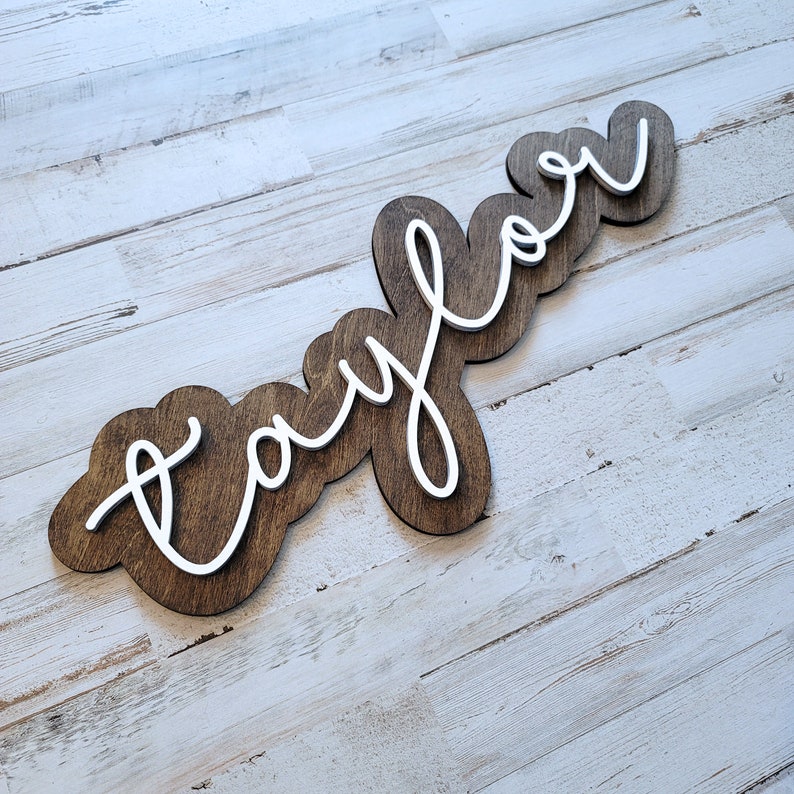 May include: A wooden sign with the word "Taylor" written in white cursive lettering. The sign is brown and has a rustic look.