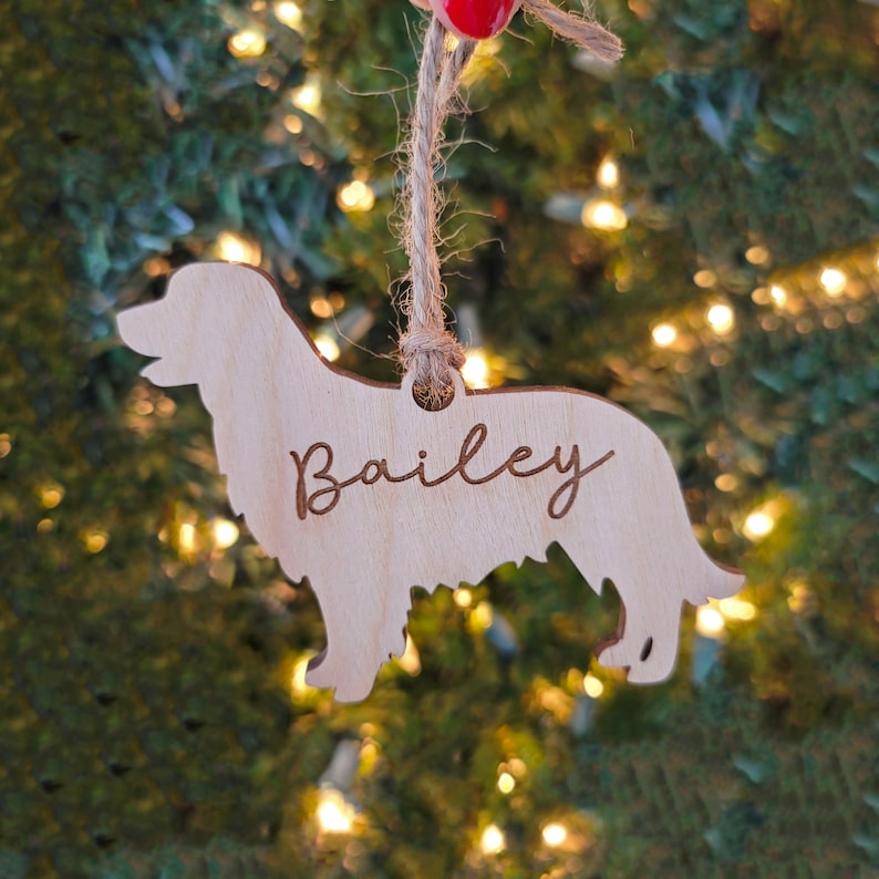May include: Wooden Christmas ornament shaped like a dog with the name "Bailey" engraved on it. The ornament is hanging on a Christmas tree.