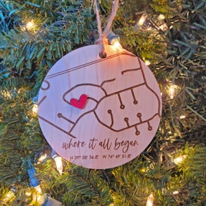 May include: A wooden Christmas ornament shaped like a map with a red heart in the center. The ornament reads "where it all began" and includes the coordinates "N 39° 58' 36.8" W 74° 49' 51.8"