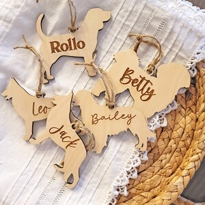 May include: Five wooden dog ornaments with names engraved on them. The names are Rollo, Betty, Leo, Jack, and Bailey.