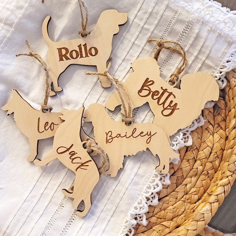 May include: Five wooden dog ornaments with names engraved on them. The names are Rollo, Betty, Leo, Jack, and Bailey.