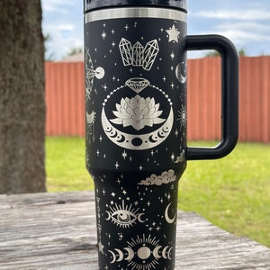 May include: Black stainless steel travel mug with a silver design of celestial and mystical symbols, including moons, stars, crystals, and an eye.