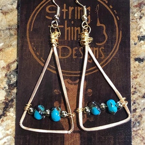 May include: A pair of handmade earrings featuring a triangular design. The earrings are crafted with gold-colored wire and adorned with turquoise and silver beads. The text "String Thing Designs" is visible on the background.