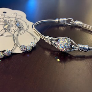 May include: A silver wire wrapped bracelet with a sparkly iridescent crystal ball charm and a matching pair of earrings with three iridescent crystal balls. The earrings are on a white card with the text "String Thing Designs".