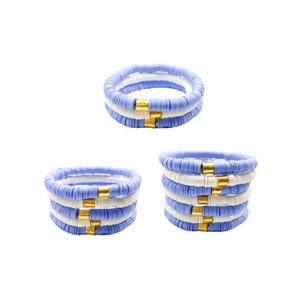 May include: A set of three blue and white beaded bracelets with gold accents. The bracelets are stacked on top of each other.