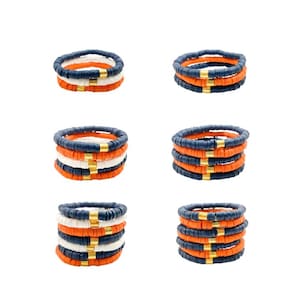 May include: Set of six stacked bracelets with orange, white, and navy blue beads. Each bracelet has a gold accent.