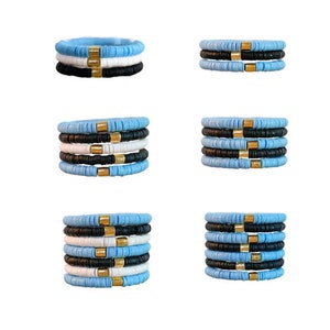 May include: Stack of six bracelets with alternating light blue, white, and black beads. Each bracelet has a gold bead spacer.