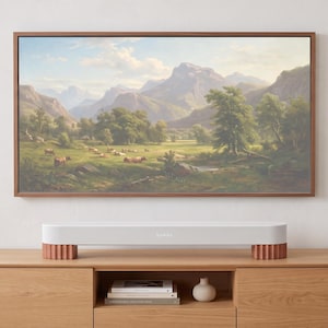 May include: A white Sonos soundbar with ribbed copper-colored feet positioned below a wall-mounted television displaying a landscape painting of a mountain range, green trees, and grazing cattle in a meadow under a bright, cloudy sky.