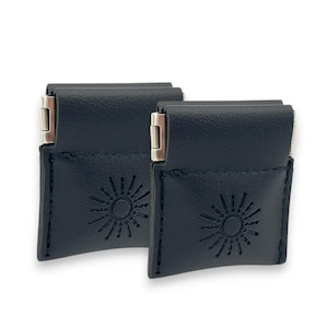 May include: Two navy blue leather pouches with a sunburst design embossed on the front. Each pouch has a silver-colored clasp. The pouches are rectangular with a flap closure.