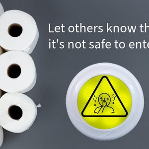 May include: A white round sign with a yellow triangle warning symbol. The symbol shows a person holding their nose with a line of wavy lines above their head. The text "Let others know that it's not safe to enter!" is written in white on a gray background. A stack of white toilet paper rolls is on the left side of the image.