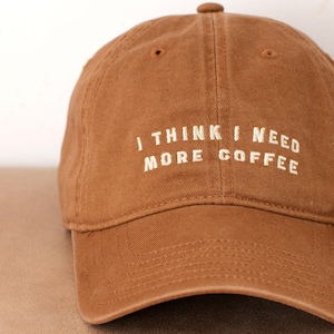 May include: A brown baseball cap with the text "I think I need more coffee" embroidered in white.