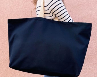 May include: A large black tote bag with cream colored handles. The bag is being held by a person wearing a striped sweater.