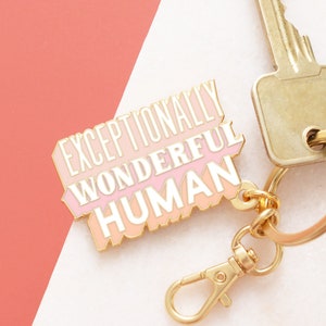 May include: Gold keychain with a pink and peach enamel charm that says "Exceptionally Wonderful Human".