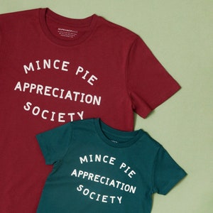 May include: Two t-shirts with the text "Mince Pie Appreciation Society" printed on them. The larger shirt is burgundy and the smaller shirt is teal.