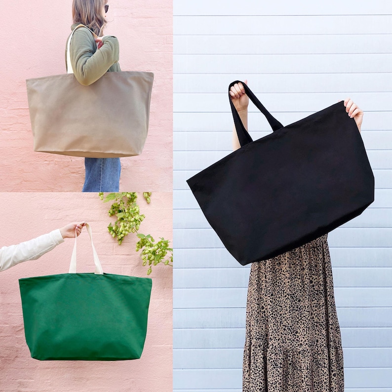 Op de afbeelding: Drie grote canvas tassen in verschillende kleuren: beige, zwart en groen. De tassen hebben brede, platte handvatten en zijn gemaakt van een stevige, natuurlijke stof.