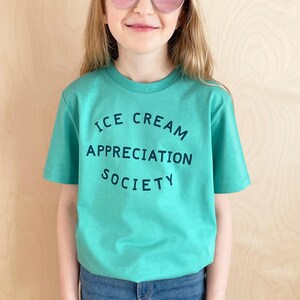 May include: A teal blue t-shirt with the text "ICE CREAM APPRECIATION SOCIETY" in a dark blue colour.