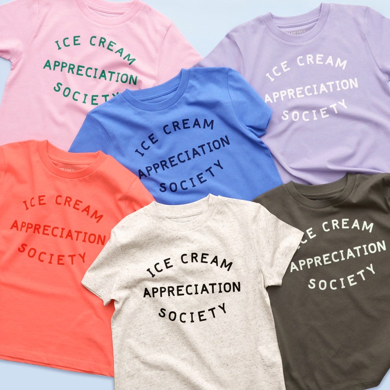 May include: Six t-shirts in different colors with the text "ICE CREAM APPRECIATION SOCIETY" printed on them. The shirts are laid out on a light blue background.