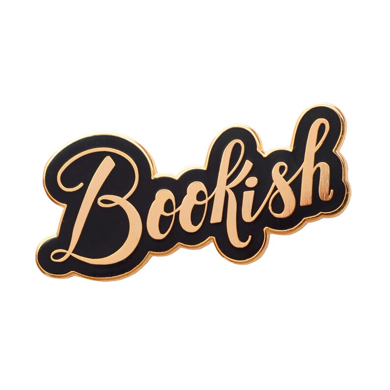 Może przedstawiać: Czarna szpilka emaliowana ze złotym napisem "Bookish".