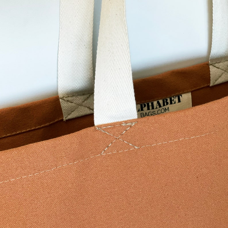 May include: A brown canvas tote bag with white straps and the text "Alphabet Bags.com" printed on the front.