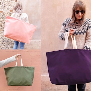 Op de afbeelding: Drie grote canvas tassen in verschillende kleuren: roze, paars en groen. De tassen hebben witte handvatten en zijn gemaakt van stevig canvas materiaal.