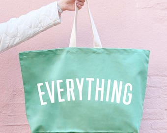 May include: A large, light green tote bag with white canvas handles. The bag has the word "EVERYTHING" printed in white on the front.