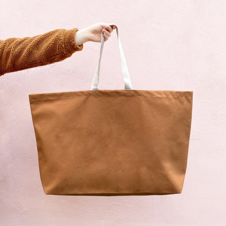 May include: A brown canvas tote bag with white straps. The bag is large and has a wide opening.