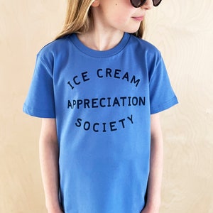 May include: A blue short-sleeved t-shirt with the text "ICE CREAM APPRECIATION SOCIETY" printed on the front.