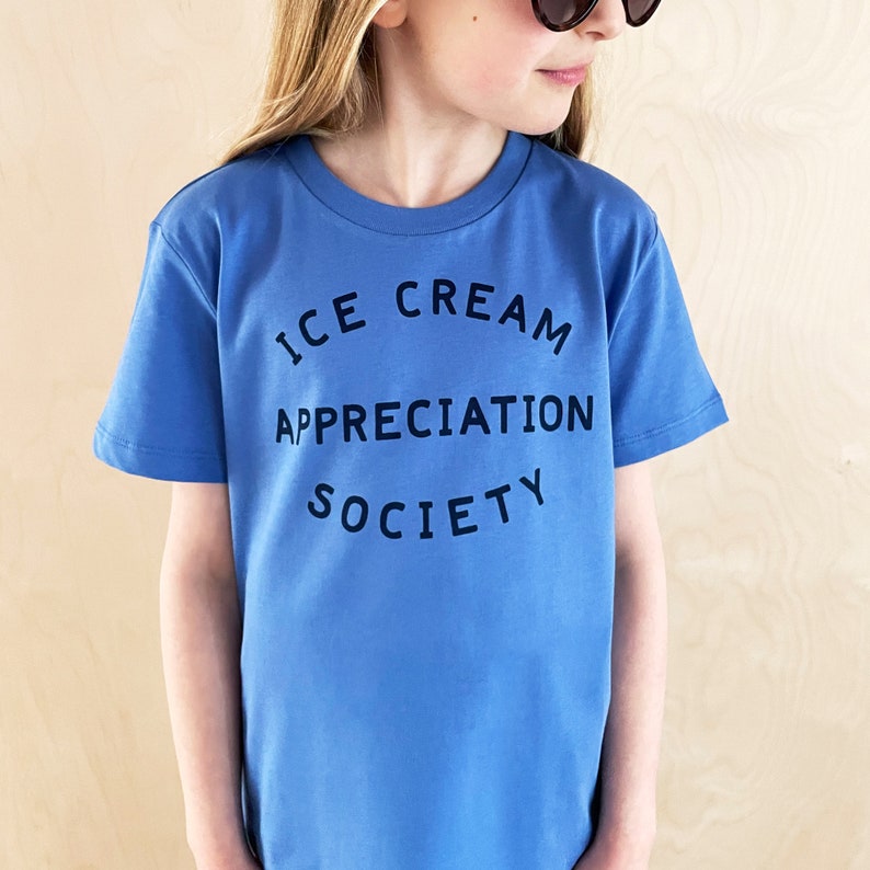 May include: A blue short-sleeved t-shirt with the text "ICE CREAM APPRECIATION SOCIETY" printed on the front.