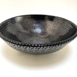 May include: A large black ceramic bowl with a textured, woven pattern. The bowl is round and has a wide, shallow opening.