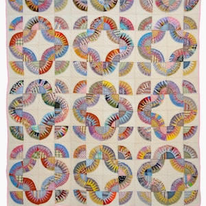 May include: A handmade quilt with a repeating pattern of colorful, curved shapes. The quilt features a cream-colored background with a pink border. The curved shapes are made of various patterned fabrics in shades of red, blue, yellow, and purple.