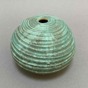 May include: A spherical, teal-colored ceramic vase with a textured, ridged surface. The vase has a small opening at the top and a weathered appearance. The decorative item is suitable for home decor.