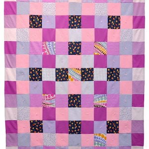 May include: A patchwork quilt made of various fabrics in shades of pink, purple, and blue. The quilt is made up of squares of different patterns, including stripes, polka dots, and floral prints.