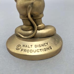 Op de afbeelding: Een gouden beeldje van Mickey Mouse dat op een voet staat met de tekst "&copy; WALT DISNEY PRODUCTIONS" erop gegraveerd.