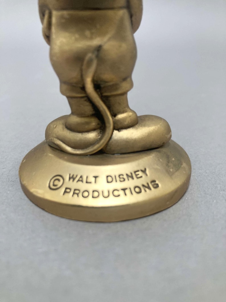 Op de afbeelding: Een gouden beeldje van Mickey Mouse dat op een voet staat met de tekst "&copy; WALT DISNEY PRODUCTIONS" erop gegraveerd.
