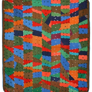 May include: A patchwork quilt with a vibrant mix of colors and textures. The quilt features a variety of fabrics in shades of brown, green, blue, orange, and red, arranged in a geometric pattern. The edges are finished with a blue border.