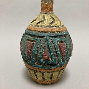 May include: A small, round ceramic vase with a textured surface. The vase is decorated with geometric patterns in shades of yellow, orange, blue, and red.
